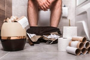 Uomo in bagno con numerosi rotoli della carta igienica finiti. Dissenteria