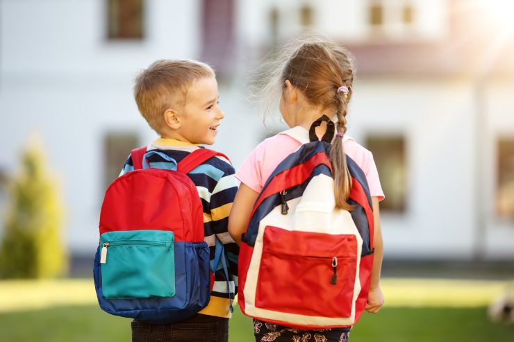 bambino e bambina vanno a scuola zaini in spalla