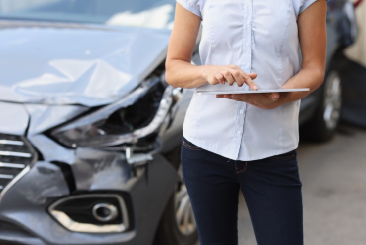 Donna che compila una contestazione amichevole con il tablet e auto incidentata sullo sfondo