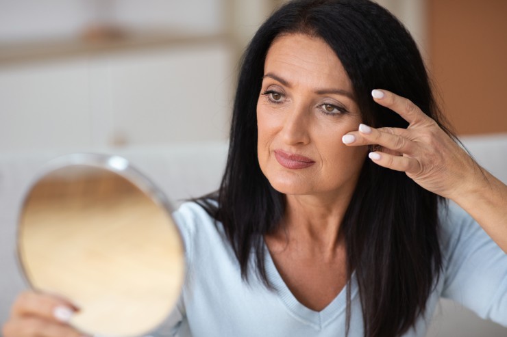 Donna over 40 che si guarda il viso allo specchio
