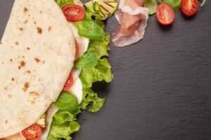 Piadina ripiegata con farcia: insalata, mozzarella, pomodori e prosciutto crudo