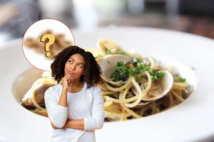 donna che pensa, ingrediente segreto e come sfondo un piatto di spaghetti alle vongole